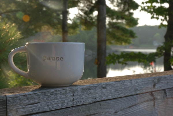 Cup of coffee on a wooden rail tie wall with lake and trees behind it