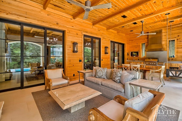 Luxury Back Porch With Wood Paneled Walls And Ceiling Black Steel And Glass Sliding Doors Seating Area Dining Area And Large Outdoor Kitchen With Built In Grill And Sink