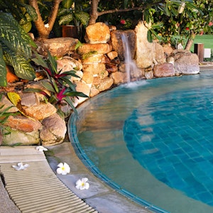 Beautiful luxury pool for your custom home with waterfall feature, blue tile, and tropical plants