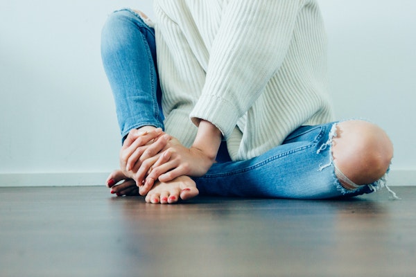 Woman sitting on the floor barefoot with jeans with ripped out knees and a white sweater