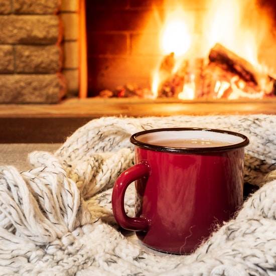 Cozy fireplace with roaring fire and a blanket with a cup of hot cocoa in the foreground.