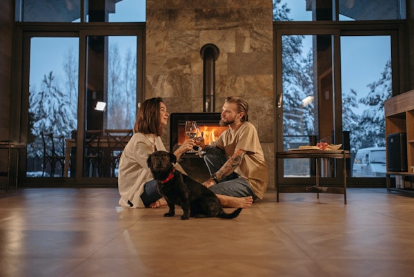 Couple and dog sitting on floor in front of a wood-burning fireplace